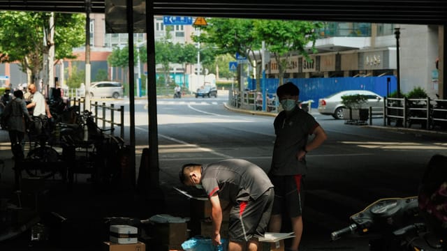 Merchants working on a sidewalk under a bridge in Shanghai, China.