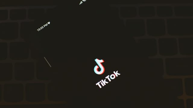 Close-up of a smartphone displaying the TikTok app logo against a dark keyboard background.