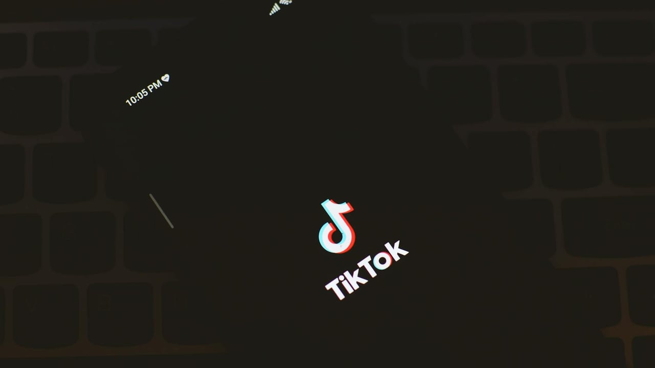 Close-up of a smartphone displaying the TikTok app logo against a dark keyboard background.