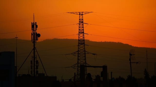 Power lines silhouetted against an orange sunset sky, conveying energy and tranquility.