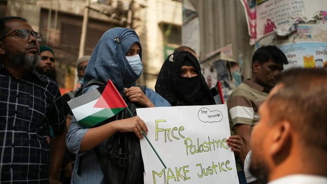 Demonstrators in Dhaka hold banners and Palestinian flags at a pro-Palestinian protest.