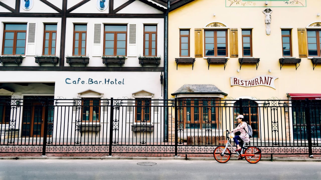 A cyclist rides by European-style buildings with cafe and hotel signs in Beijing on a sunny day.