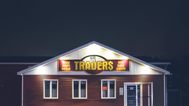 Illuminated trader's storefront at night displaying vibrant signage with business motifs.