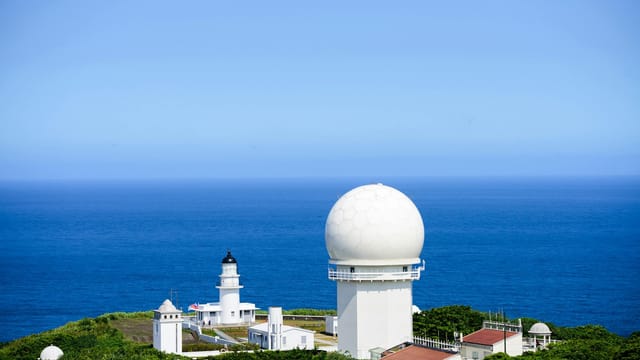 Stunning aerial shot of Sandiaojiao Lighthouse against a clear blue sky and expansive ocean.