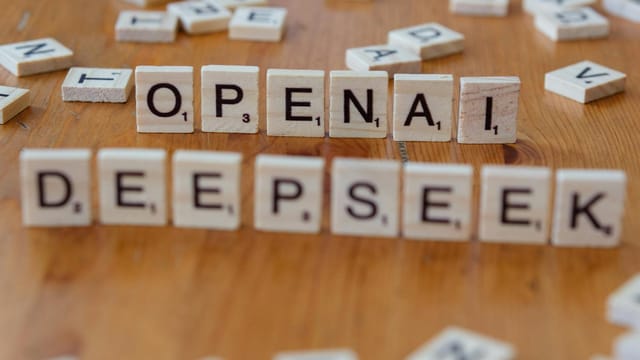 Close-up of wooden Scrabble tiles spelling OpenAI and DeepSeek on wooden table.