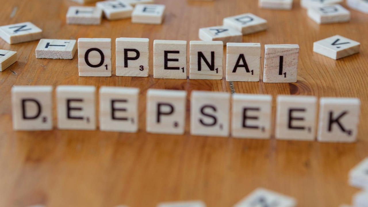 Close-up of wooden Scrabble tiles spelling OpenAI and DeepSeek on wooden table.