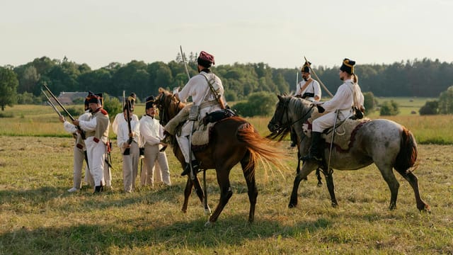 Reenactment of historical military horseback and infantry in outdoor setting.