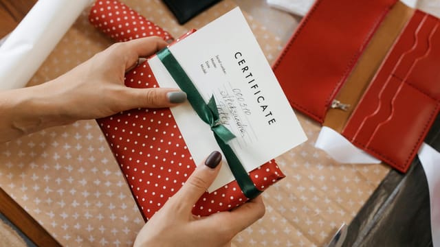 Close-up of hands holding a gift certificate wrapped in red polka dot paper and green ribbon.