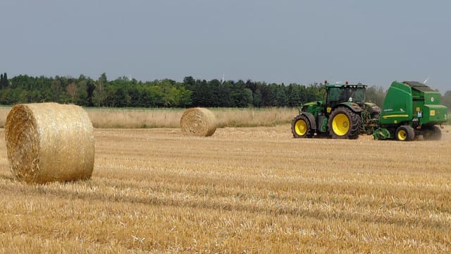 A green tractor baling straw outdoors in a field near Neuss, Germany.