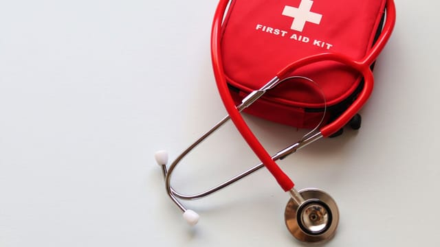A red first aid kit paired with a stethoscope, signifying healthcare and medical treatment essentials.