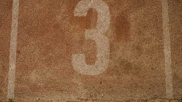 Close-up of a textured running track with the number three, showcasing sport simplicity and earthy tones.