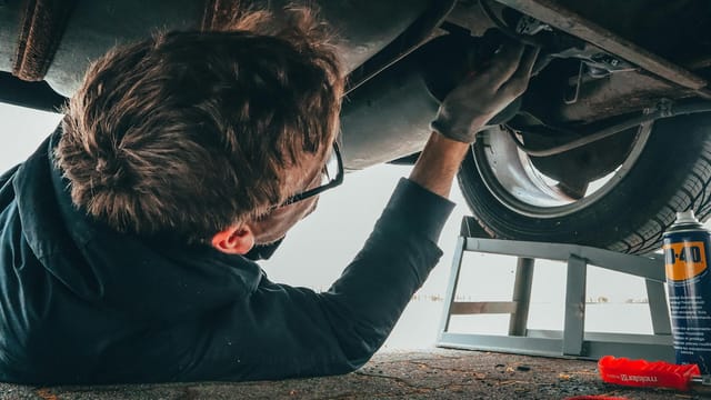 Mechanic skillfully repairing car undercarriage in outdoor setting with tools.