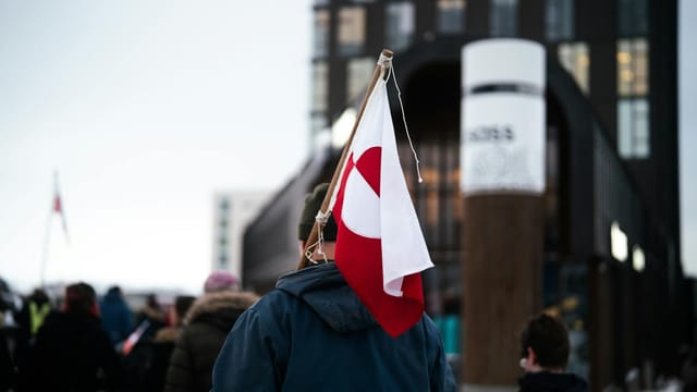 A protestor holding the Greenland flag amidst a crowd in Nuuk, Greenland.