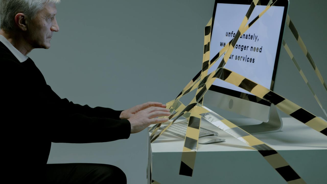 Elderly man at computer with termination notice, facing unemployment.