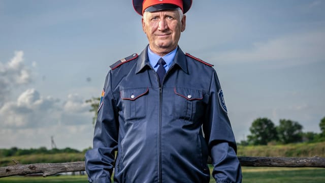 Elderly man wearing official uniform poses confidently outside on a sunny day.