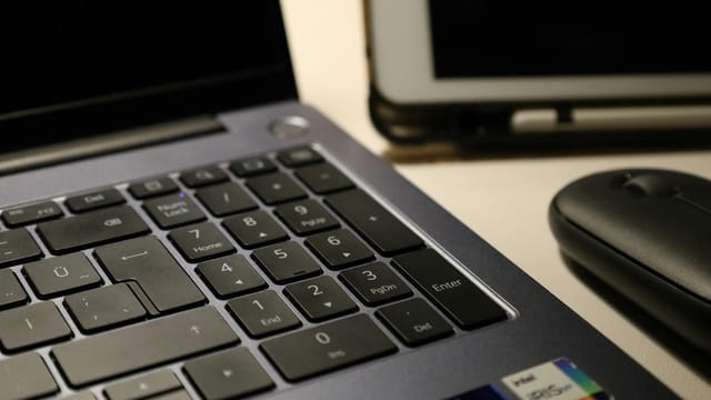 Close-up of laptop keyboard, wireless mouse, and tablet illustrating modern workspace technology.