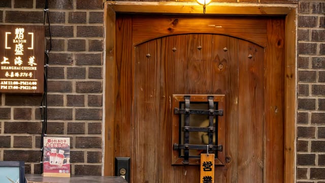 Warmly lit wooden door entrance of a Shanghai cuisine restaurant with vintage signage.
