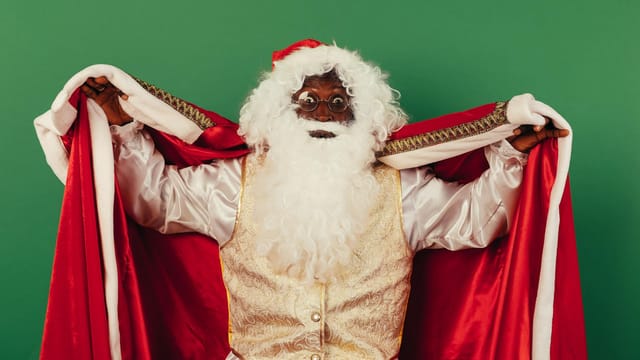 Black Santa Claus in traditional costume spreading festive joy with a surprised expression.