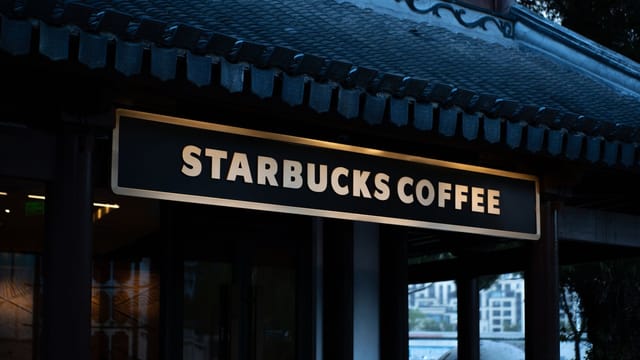 Starbucks coffee shop sign displayed on a building with traditional design elements, captured at dusk.