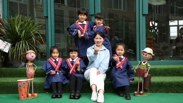 Group of children in blue graduation uniforms posing with a teacher outdoors.