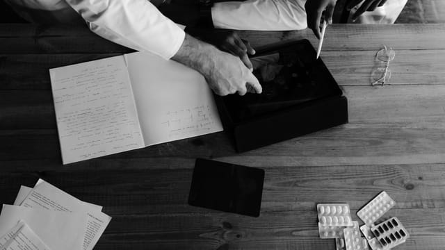Doctors collaborating on medical research using tablets and notebooks in a monochrome setting.