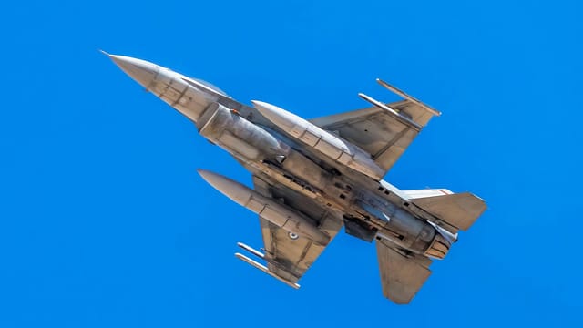 F-16 military jet flying under clear blue skies, showcasing maneuverability and power.