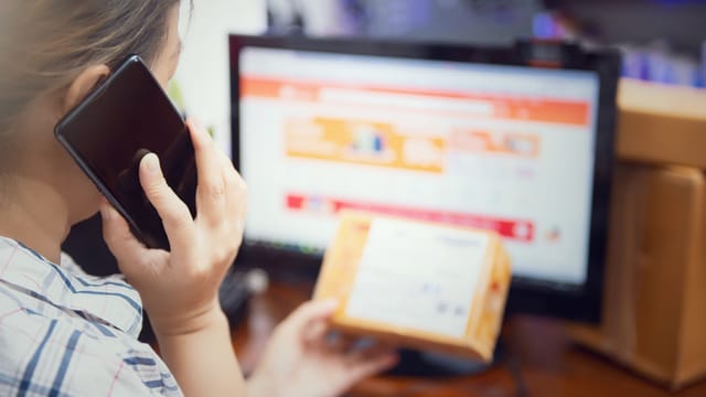 Woman multitasking by using a phone and checking an online purchase package at home.