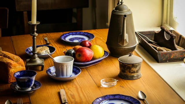 A rustic kitchen table scene with fruits, vintage utensils, and ceramic dishes.