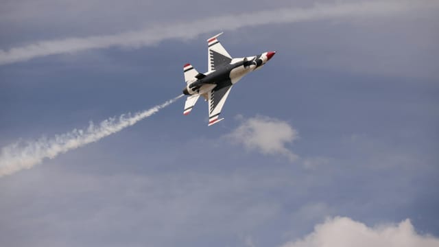 Jet fighter flying at high speed with vapor trails against a blue sky.