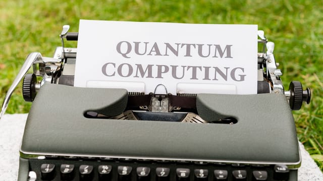 A typewriter with 'Quantum Computing' text outdoors on grass, blending old and new technologies.