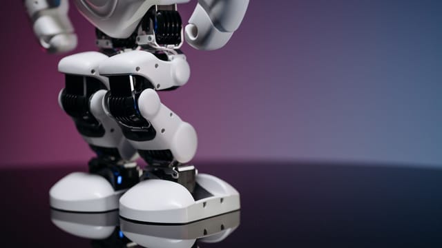 A detailed close-up image of a modern robot's legs and feet, reflecting on a glossy surface.
