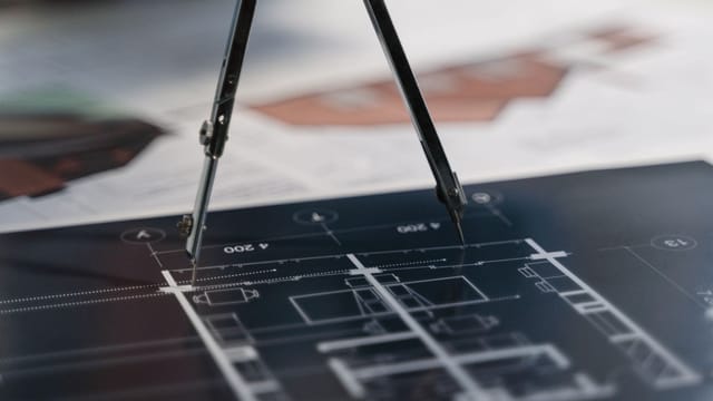 A compass on architectural blueprints, showcasing planning and measurement details.