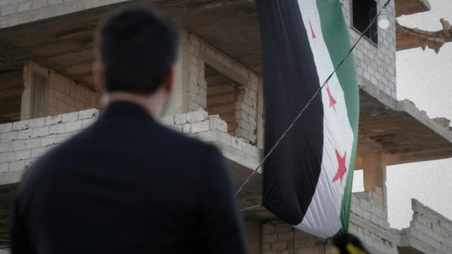 A man observes a Syrian flag draped over a war-torn building in Damascus, Syria.