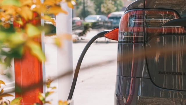 Close-up of an electric car charging at a station with blurred cars in the background.