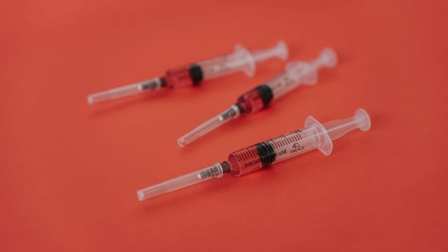 Three syringes with red liquid on a bold red surface, featuring medical themes.