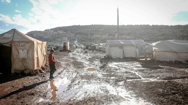 Muddy campsite in Idlib, Syria showcasing temporary shelters and difficult living conditions.