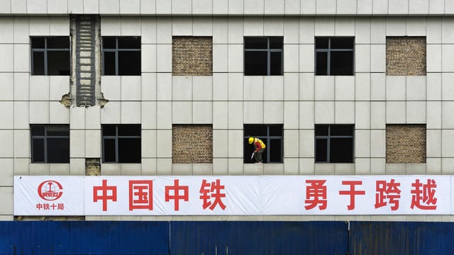 A construction worker on a building facade with a Chinese sign in the foreground.