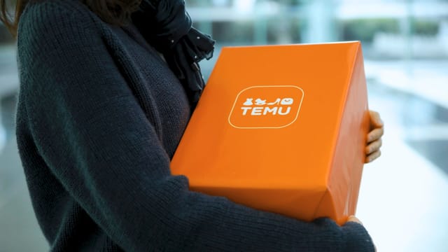 A person holding an orange TEMU box, symbolizing online shopping and delivery indoors.