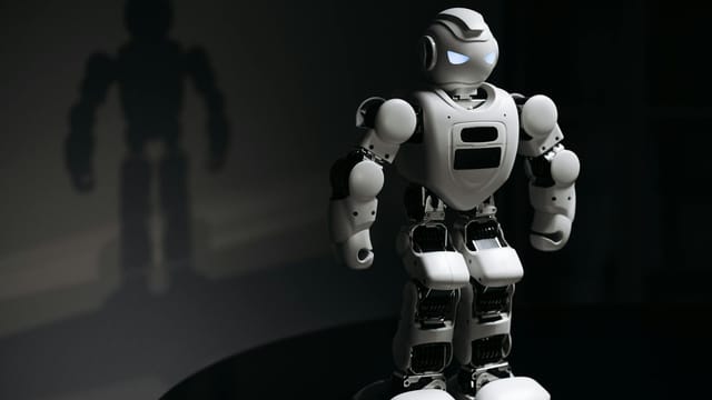 White robot toy casting a shadow in a dark studio setting, highlighting artificial intelligence.