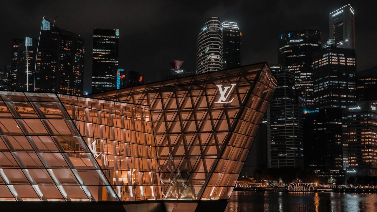 Captivating night view of Singapore skyline with iconic Louis Vuitton architecture reflected on water.