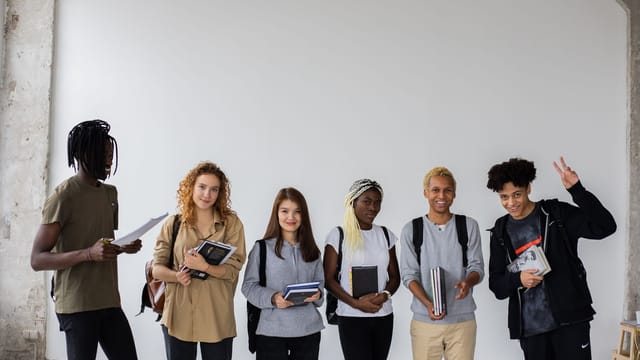 Group of African American man showing peace gesture while standing with diverse classmates holding documents and notebooks