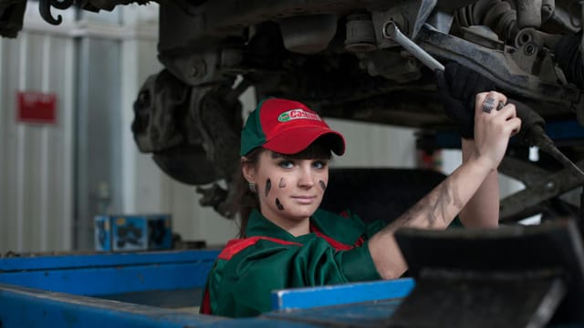 Female mechanic maintaining a car in an auto repair shop, showcasing skill and concentration.