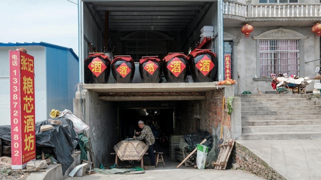 Street view of a traditional Chinese liquor workshop with large jars and man working inside.