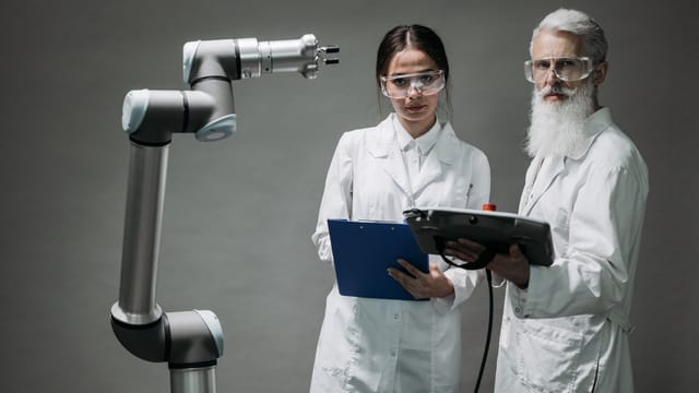 Two scientists in lab coats analyzing a robotic arm in a laboratory setting.
