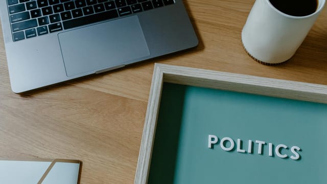 A contemporary workspace featuring a laptop, coffee cup, and a sign with the word 'Politics'.