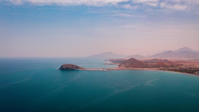 Drone view of city next to mountain range on coast of calm blue endless ocean