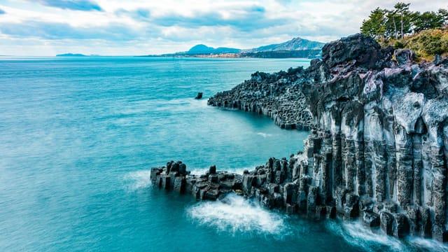 A breathtaking view of Jeju's volcanic cliffs with turquoise waters and dramatic scenery.