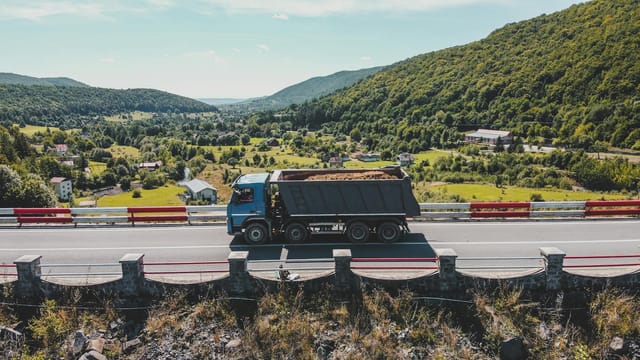 Blue truck driving on a mountain highway in Romania, with a scenic landscape view.