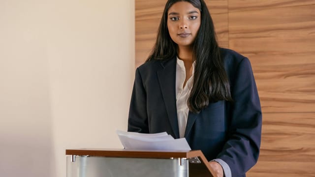 Woman in a suit presenting at a podium, symbolizing leadership and empowerment.