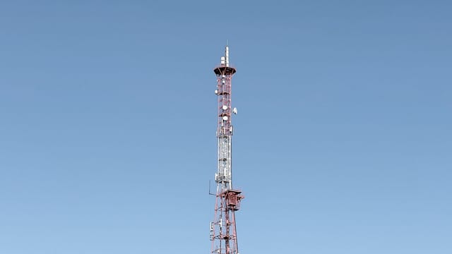 A tall communication tower set against a cloudless blue sky, symbolizing modern telecommunications.